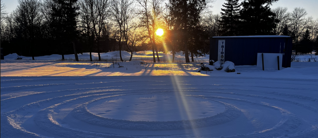 Snow in a concentric circle pattern formed by a ski trail groomer with a sunset in the background
